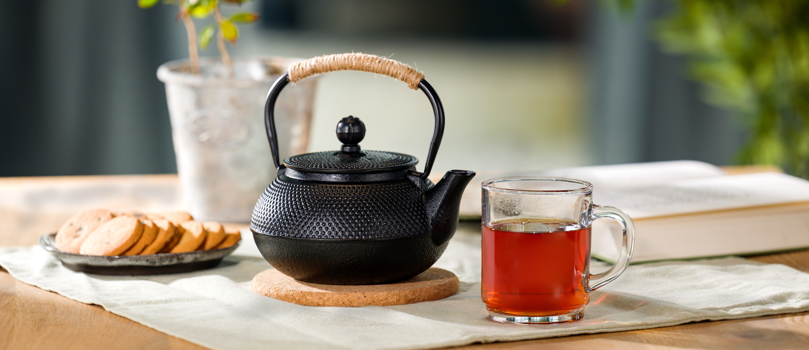 Schwarze Teekanne und Glas mit Tee auf einem gedeckten Tisch, daneben ein Teller mit Keksen