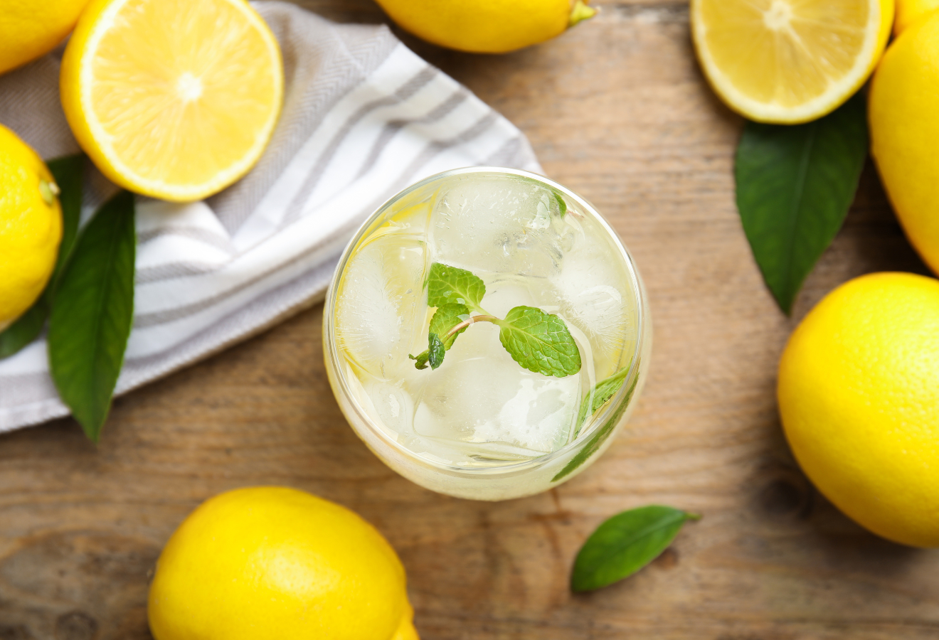 Lemon-Fizz in einem Glas mit Minzblättern, daneben Zitronen