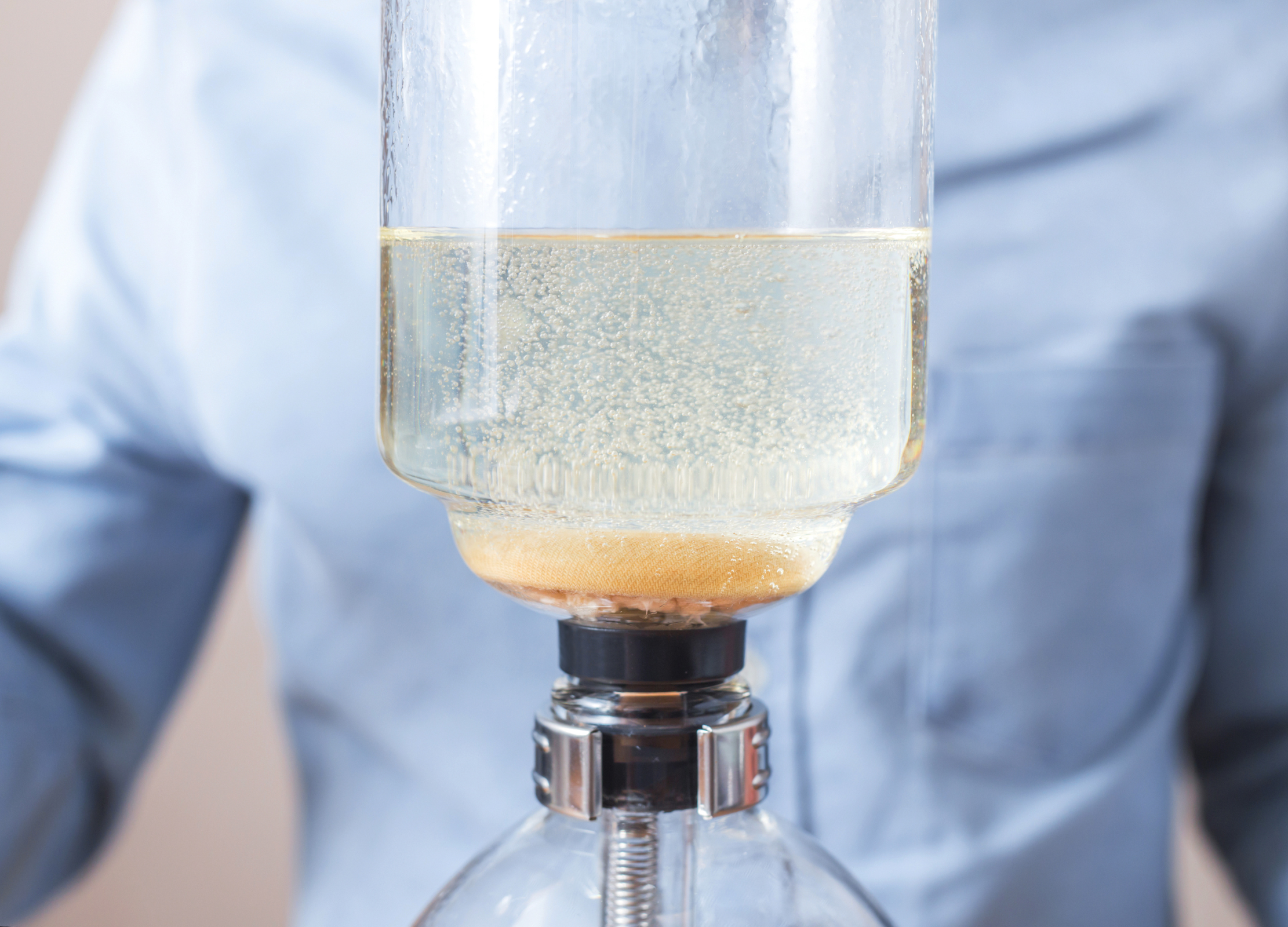 Heißes Wasser steigt im oberen Glasbehälter eines Syphon-Kaffeebereiters auf und beginnt, sich mit Kaffeepulver zu vermischen