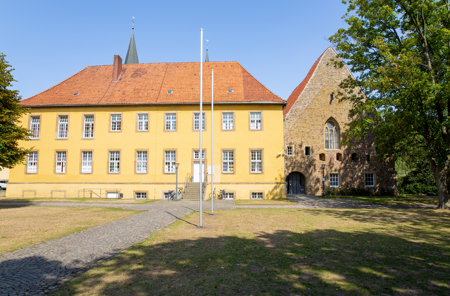 Historisches Gebäude mit gelber Fassade und rotem Dach neben einer alten Kirche aus Naturstein
