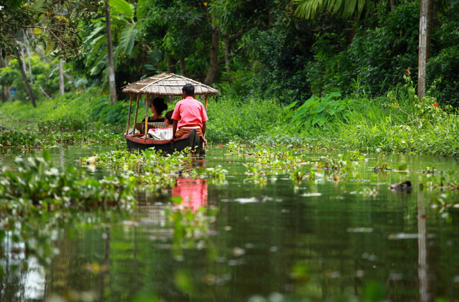 Zwei Personen in einem kleinen Boot auf einem Wasserkanal in tropischer Umgebung in Kerala