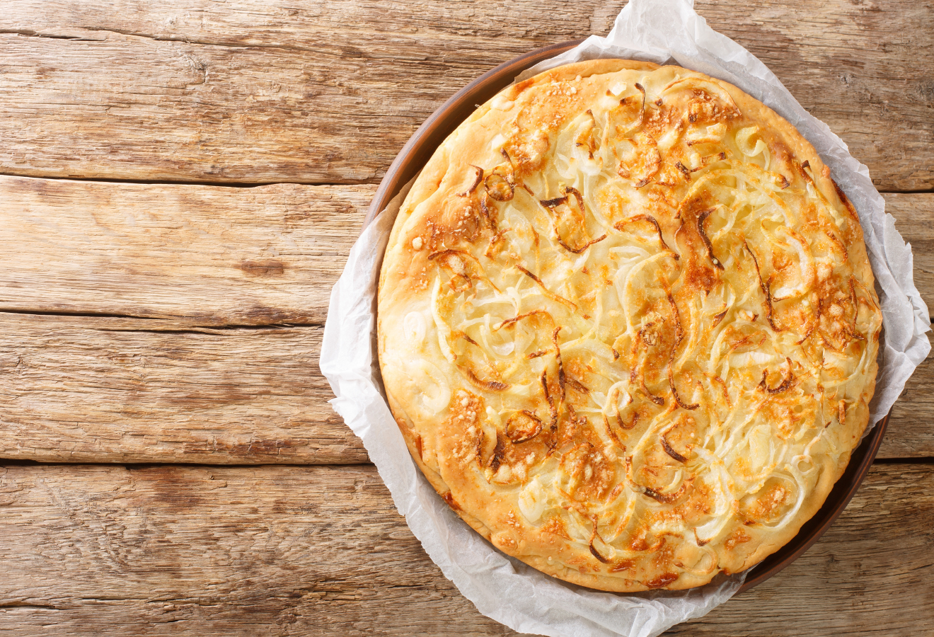 Zwiebel-Käse-Focaccia „Sahara“ auf einem Holzteller mit Backpapier