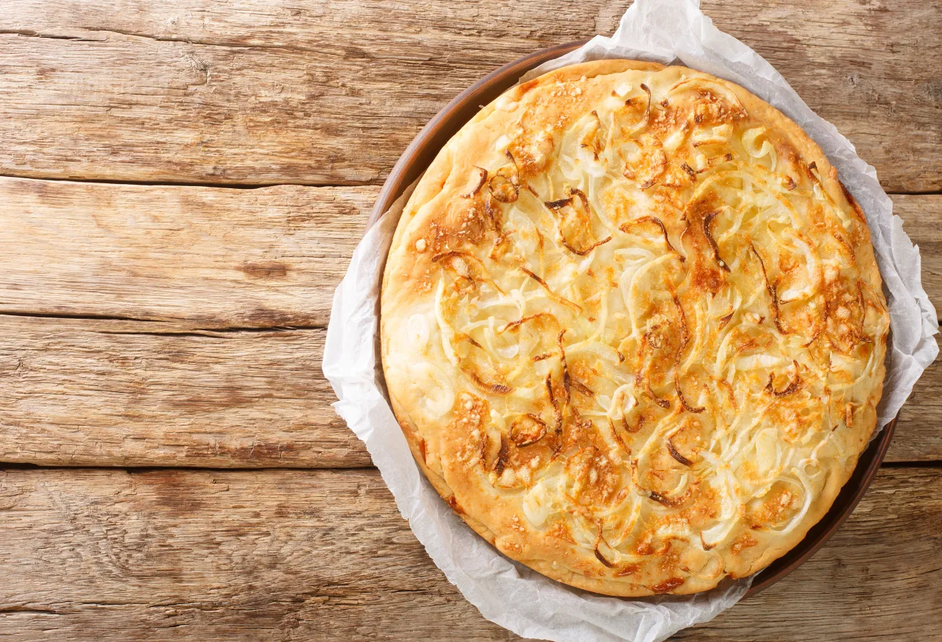  Zwiebel-Käse-Focaccia „Sahara“ auf einem Holzteller mit Backpapier