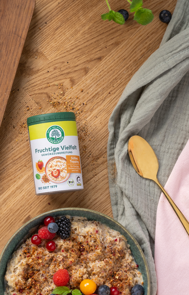 Gewürzstreuer ‚Fruchtige Vielfalt‘ neben einer Schale Porridge mit frischen Beeren und goldenem Löffel