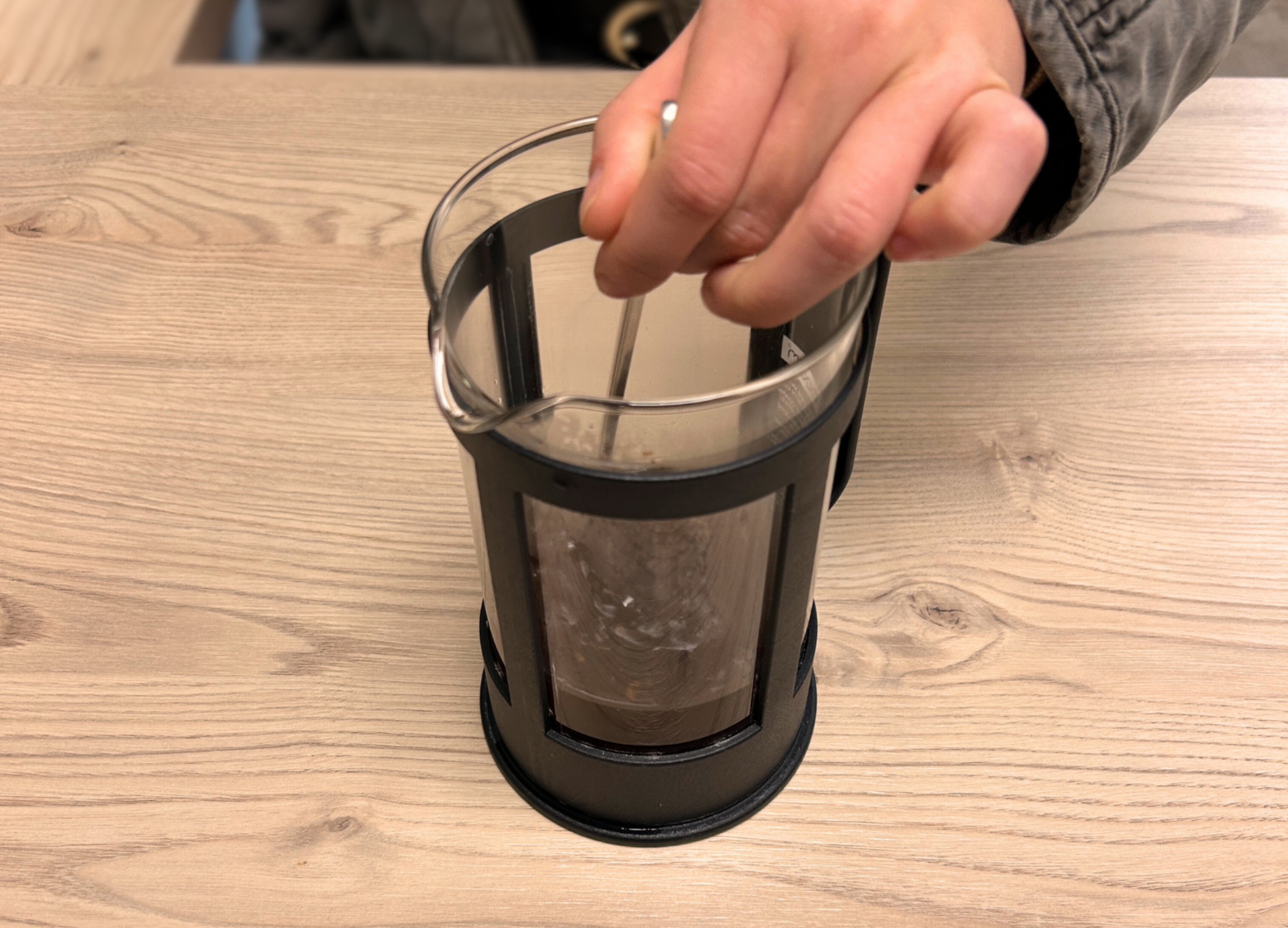 Eine Hand rührt gemahlenen Kaffee in einer French Press aus Glas um