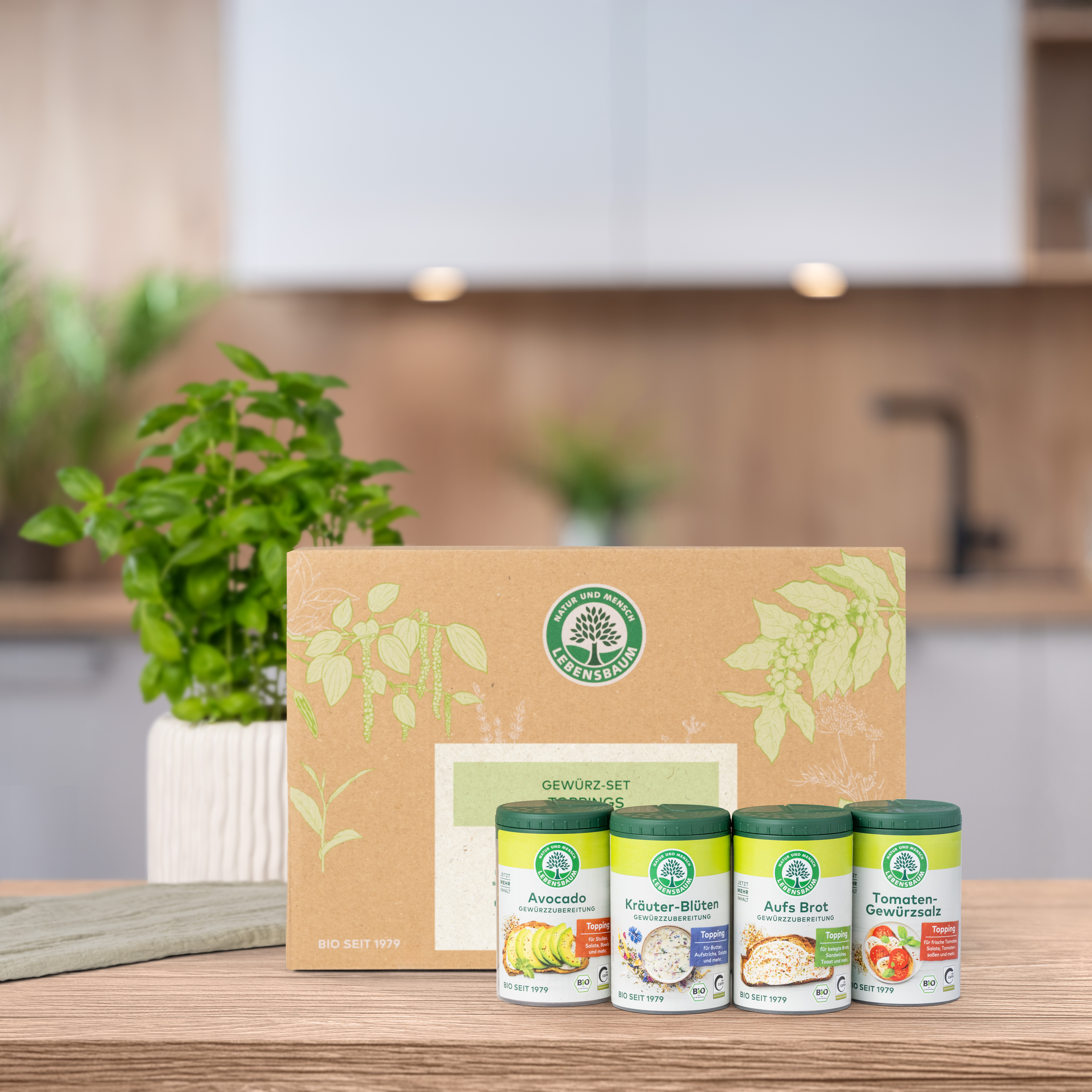 Verschlossenes Geschenk-Set steht auf einem Holztisch in der Küche. Vor der Geschenk-Set Verpackung  stehen die darin enthaltenen Produkte