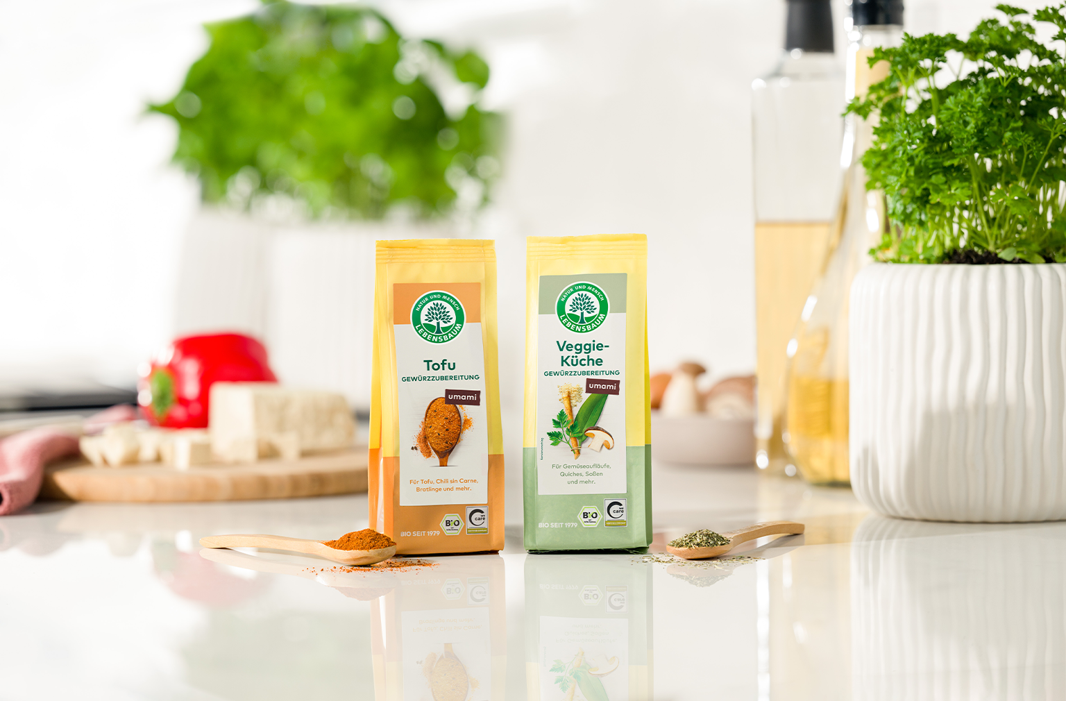 Zwei Gewürzpackungen mit der Aufschrift ‚Tofu‘ und ‚Veggie-Küche‘, daneben passende Gewürze auf Holzlöffeln