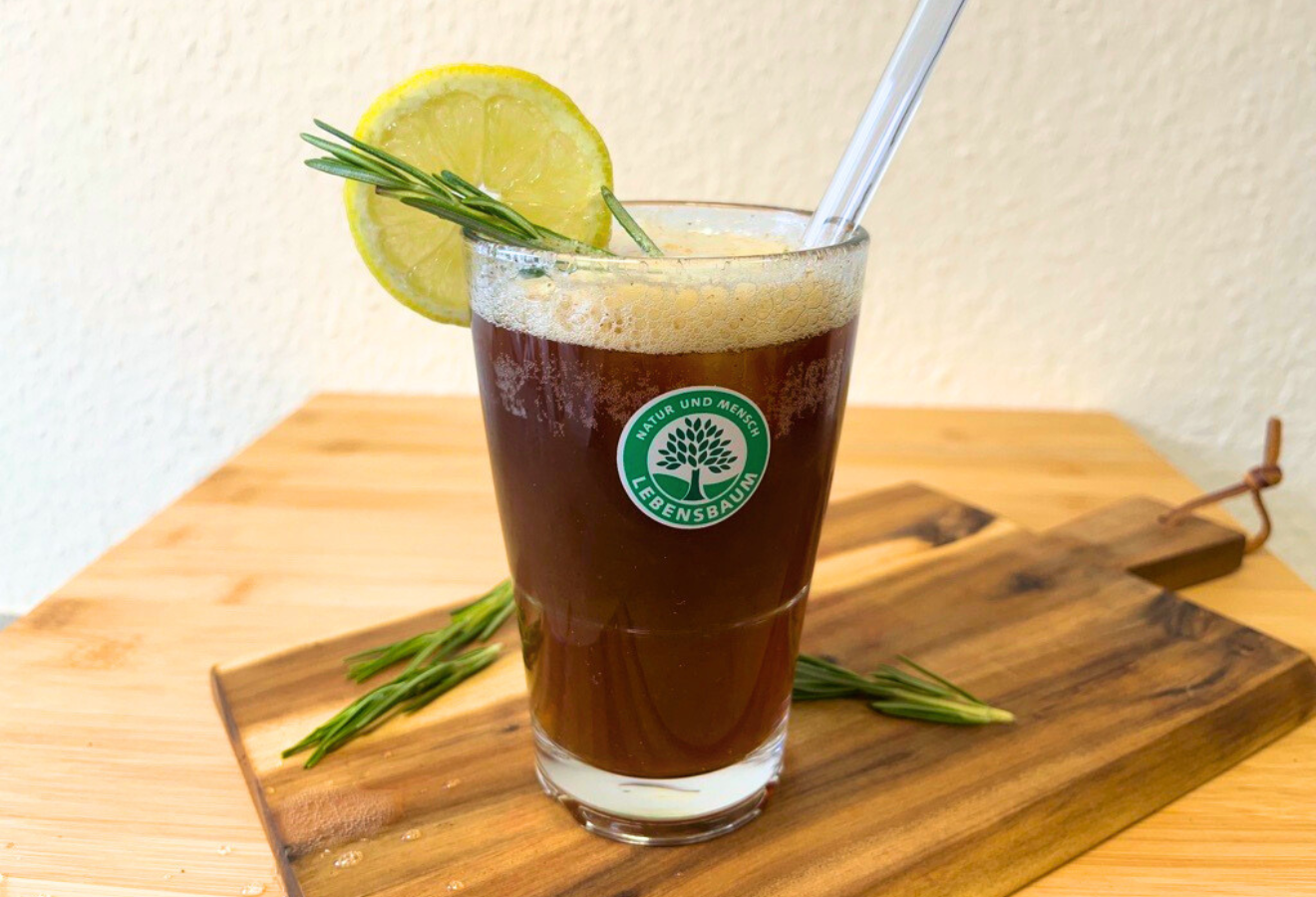 Espresso Tonic in einem Glas mit Rosmarin und einer Limettenscheibe garniert auf einem Holzbrett