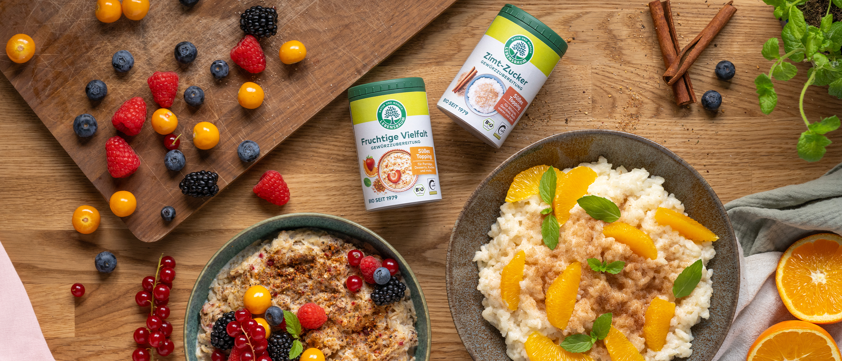 Zwei Schalen mit Porridge und Milchreis, garniert mit frischen Früchten und Gewürzen, daneben Streuer mit Zimt-Zucker und Fruchtige-Vielfalt