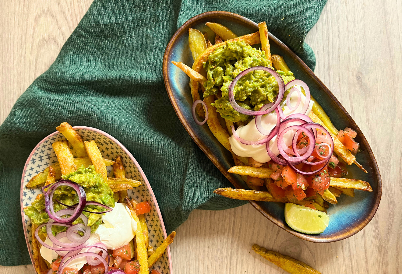 Poutine mit Guacamole, Salsa und Sour Cream auf zwei Tellern