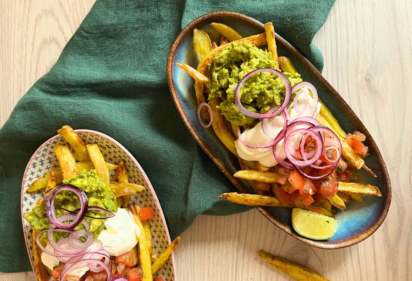 Poutine mit Guacamole, Salsa und Sour Cream auf zwei Tellern