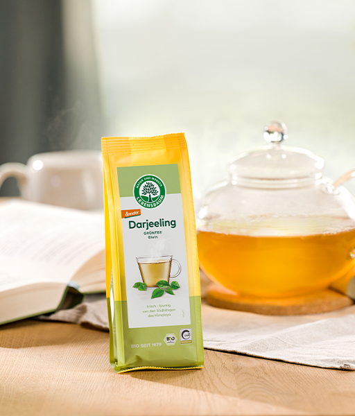 Kategoriebild für Grüntee, Verpackung von grünem Darjeeling Tee neben einer Teekanne gefüllt mit hellem echten Tee