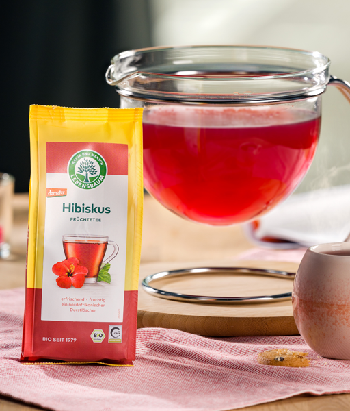 Kategoriebild für Früchtetee, Hibiskus-Verpackung neben einer Monokanne leuchtend rotem Früchtetee