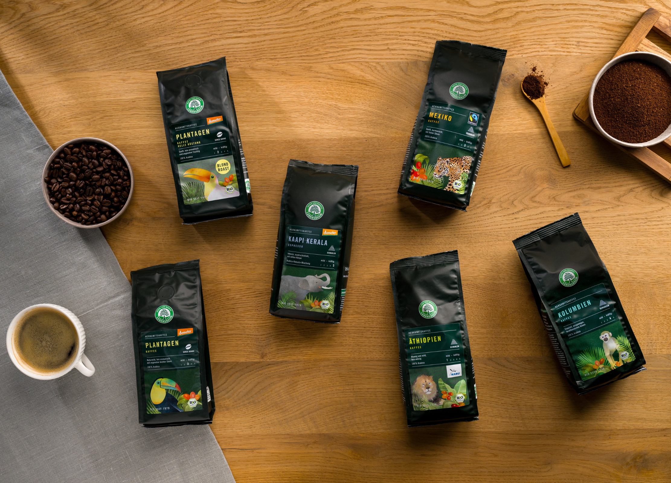 Herkunftskaffee-Serie auf einem Holztisch, daneben zwei Schüsseln, mit Kaffee Bohnen und gemahlenem Kaffee