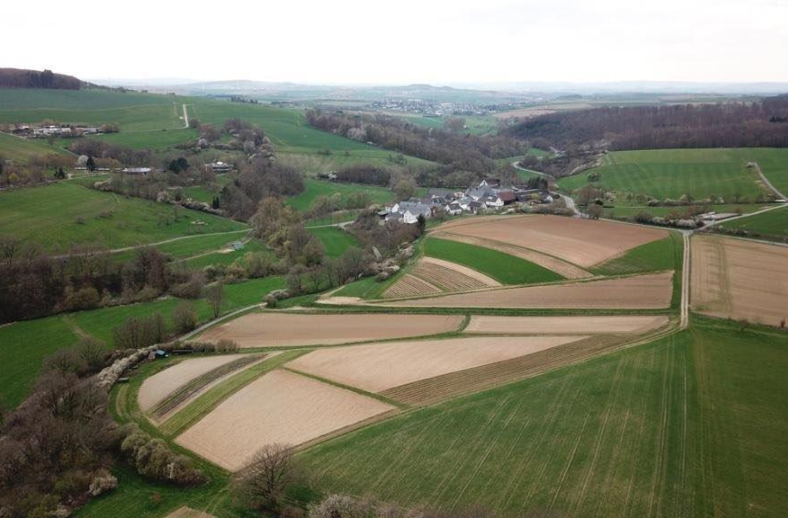 Ländliche Landschaft mit Feldern, Wiesen und dem kleinen Dorf  Hünfelde in hügeliger Umgebung
