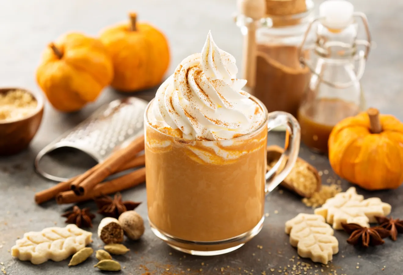 Pumpkin Spice Latte in einer Glastasse mit Sahne, im Hintergrund herbstliche Deko