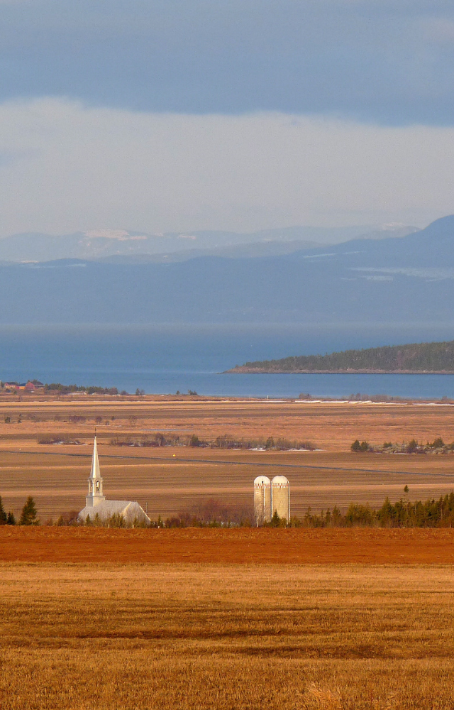 Weite Landschaft mit Feldern, einer Kirche, Silos und einem See im Hintergrund in Kanada