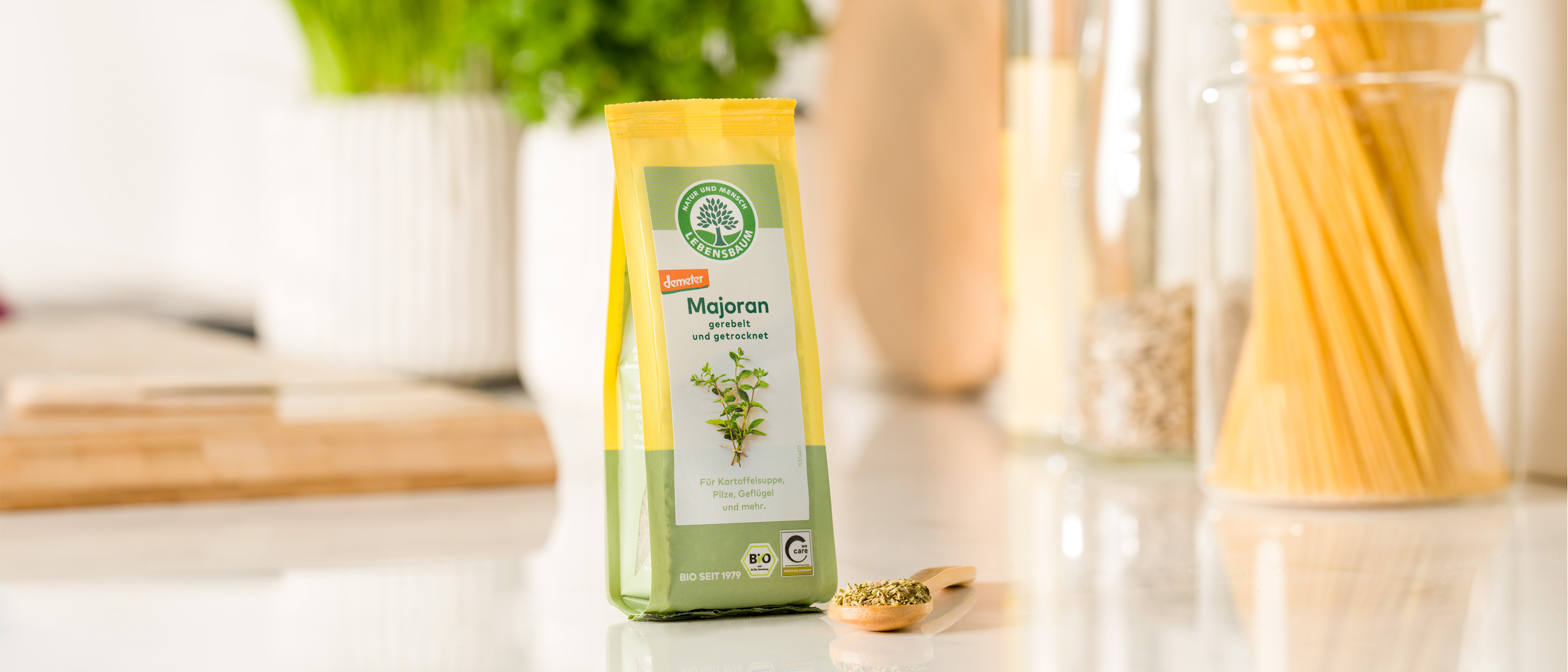 Ein Beutel Lebensbaum Majoran steht auf einer Küchenarbeitsfläche, daneben ein Holzlöffel mit getrocknetem Gewürz