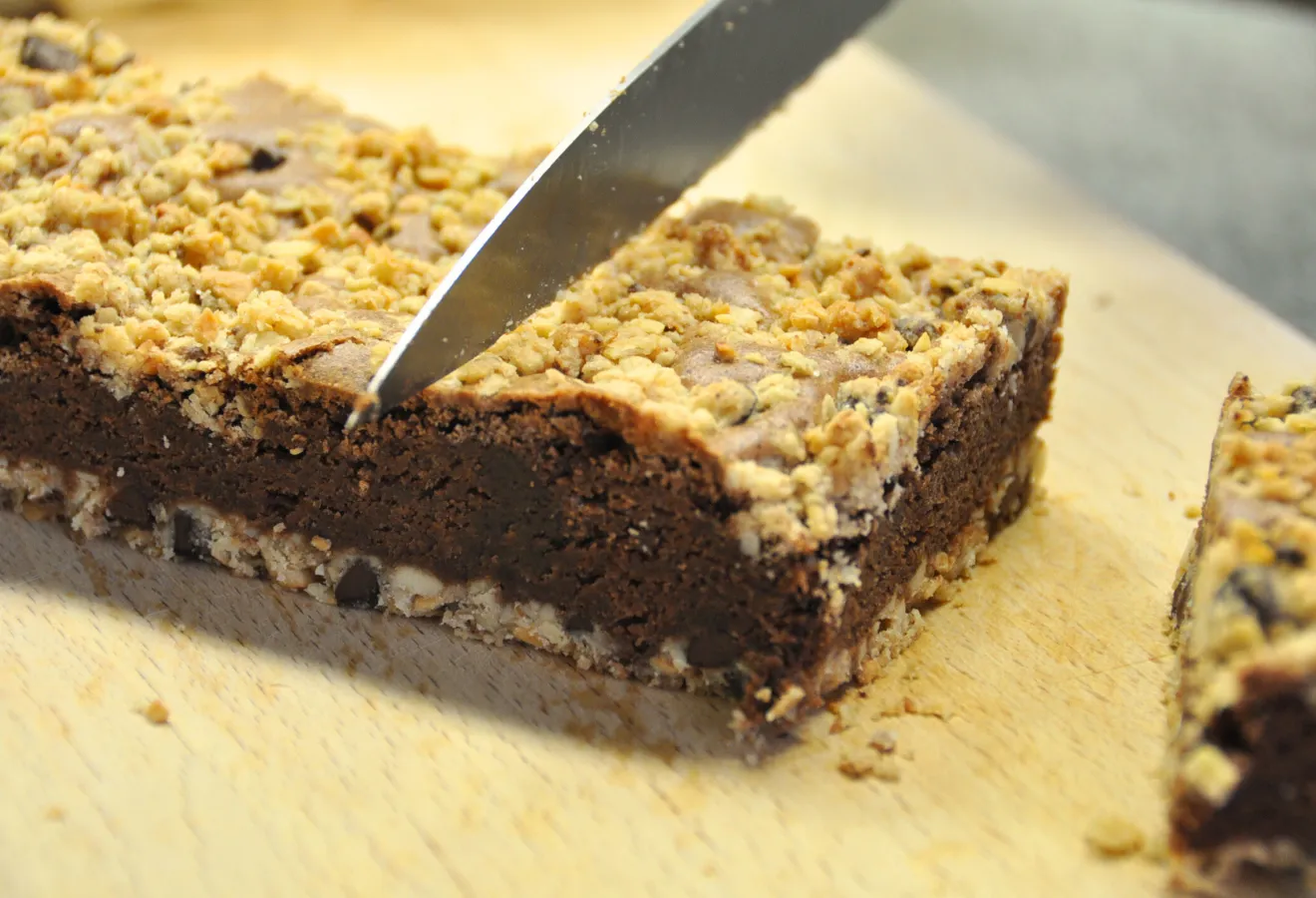 Knusper-Schoko-Brownies auf einem Holzbrett, darüber ein Messer