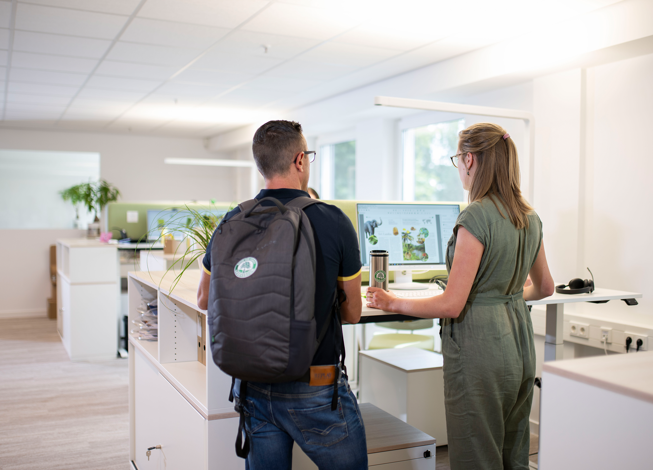 Zwei Personen stehen an einem höhenverstellbaren Schreibtisch in unserem modernen Büro in Diepholz und schauen gemeinsam auf einen Bildschirm