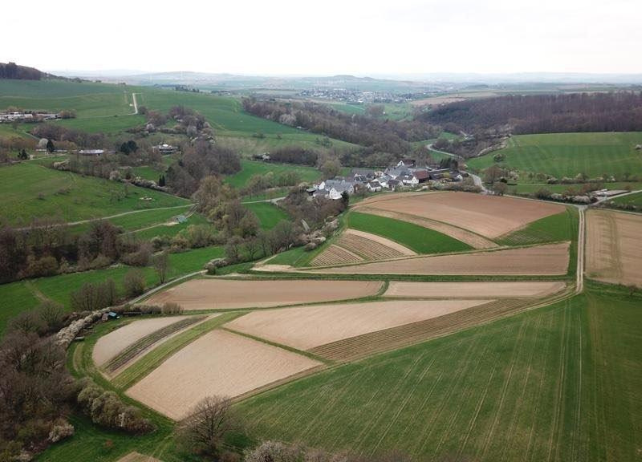 Ländliche Landschaft mit Feldern, Wiesen und einem kleinen Dorf in hügeliger Umgebung