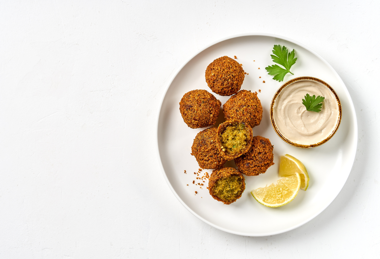 Falafel mit zitroniger Soße auf einem weißen Teller mit einer Schale Dip und Zitronenspalten daneben