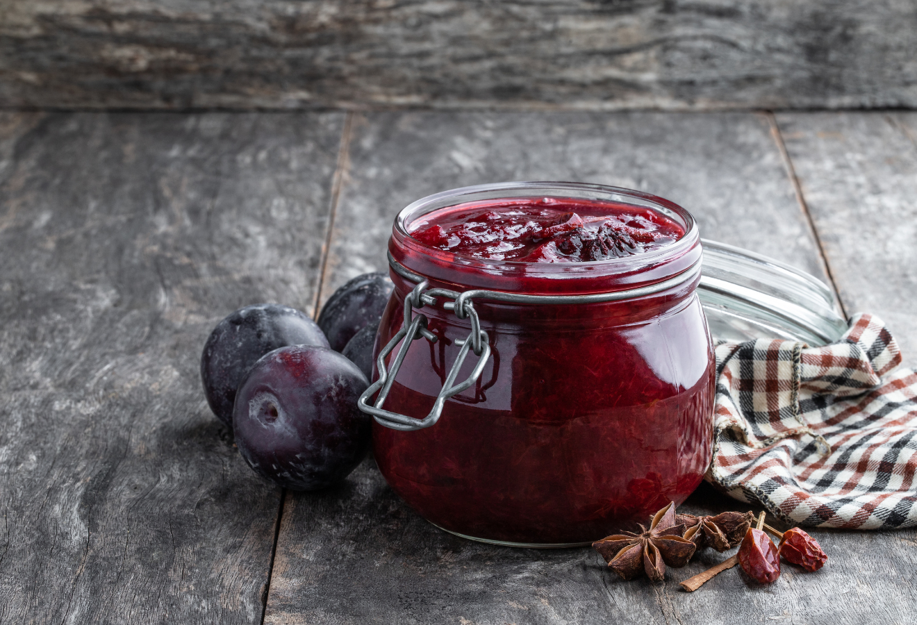 Pflaumen-Chutney im Einmachglas, daneben Pflaumen, Sternanis und Cranberries