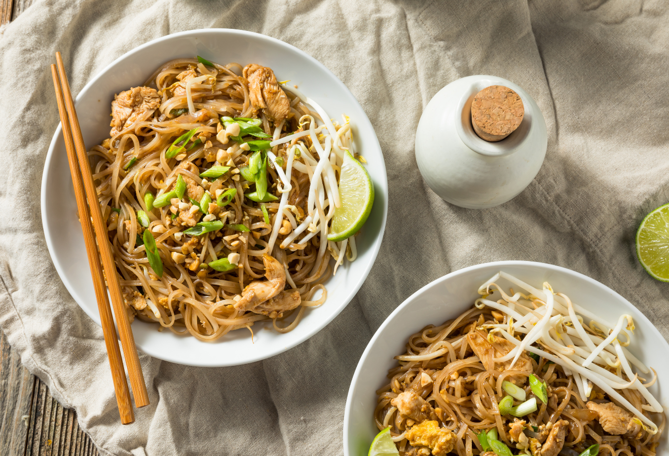 Pad Thai in zwei Schalen mit Bambussprossen und Limettenspalten garniert, darauf Essstäbchen