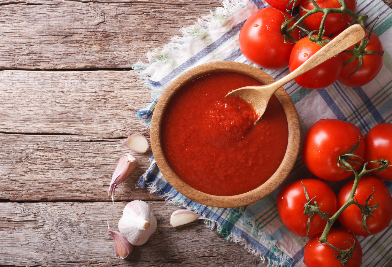 Tomaten-Estragon-Soße in einer Holzschale mit einem Holzkochlöffel darin, daneben Tomaten und Knoblauch