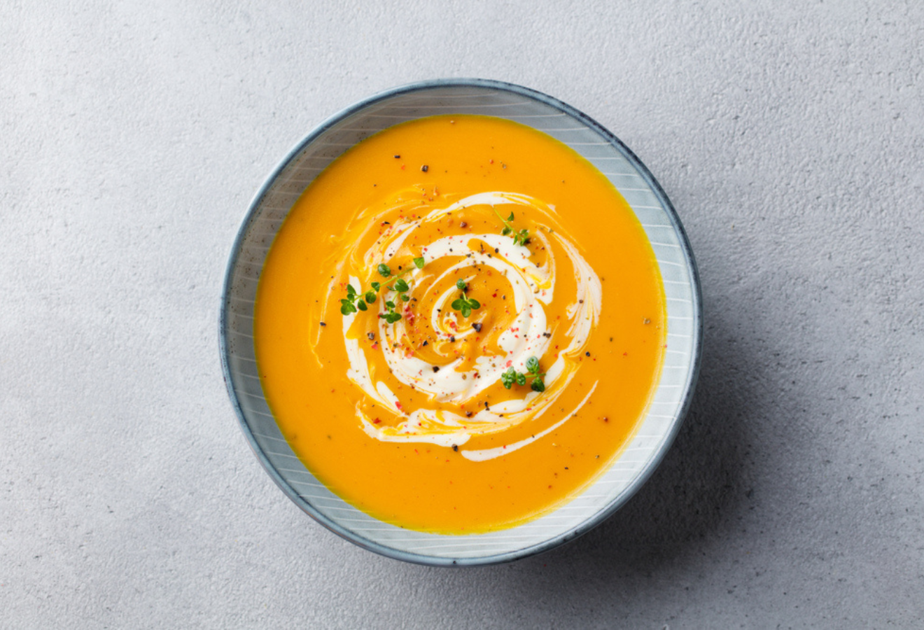 Wärmende Wintersuppe in einer blauen Schüssel mit Sahne und Kräutern garniert
