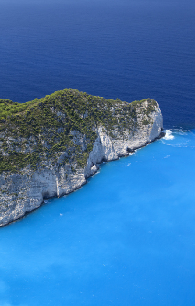 Weiße Steilküste mit dichtem Wald, umgeben von tiefblauem und türkisfarbenem Meer in Griechenland