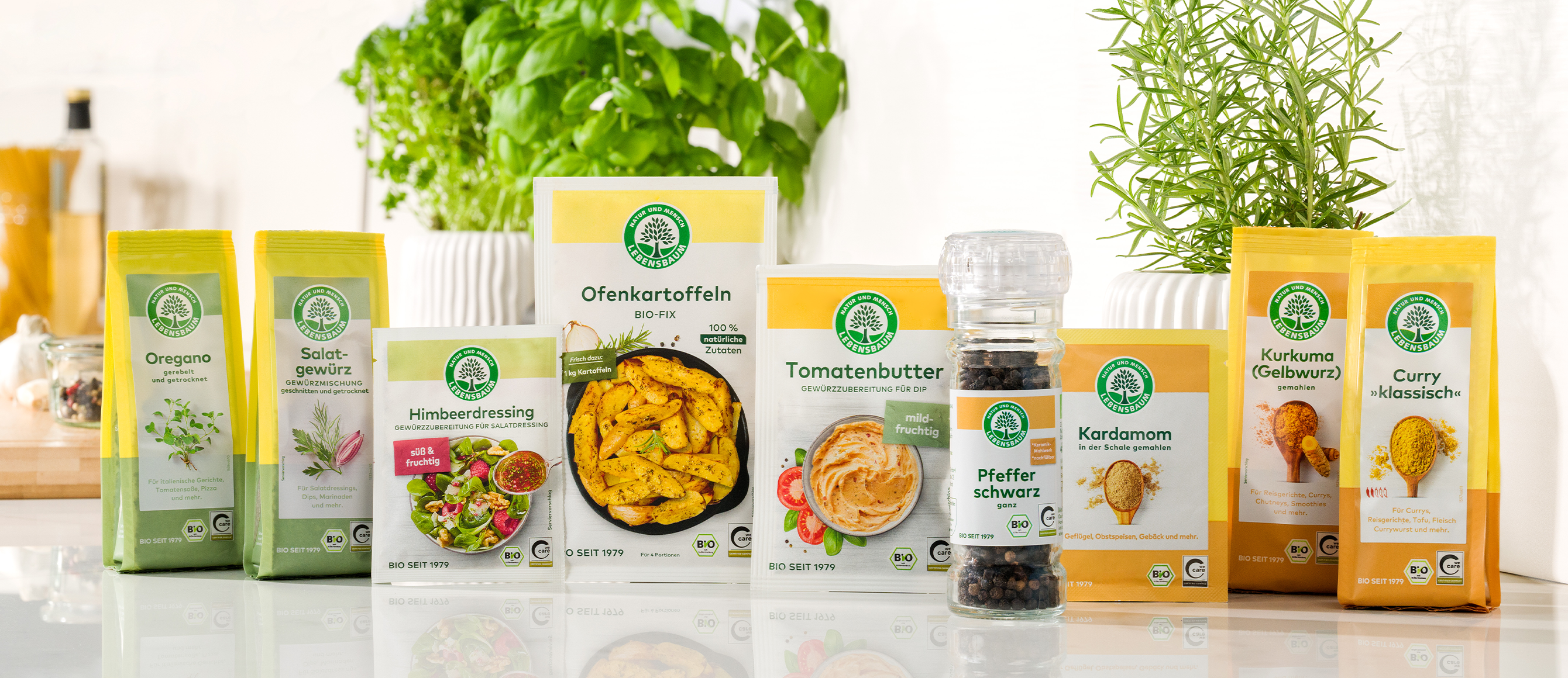 Bio-Gewürze und Gewürzmischungen: Oregano, Salbeigewürz, Himberdressing, Ofenkartoffeln, Tomatenbutter, schwarzer Pfeffer, Kardamom, Kurkuma und Curry in gelben Verpackungen mit grünem Logo.