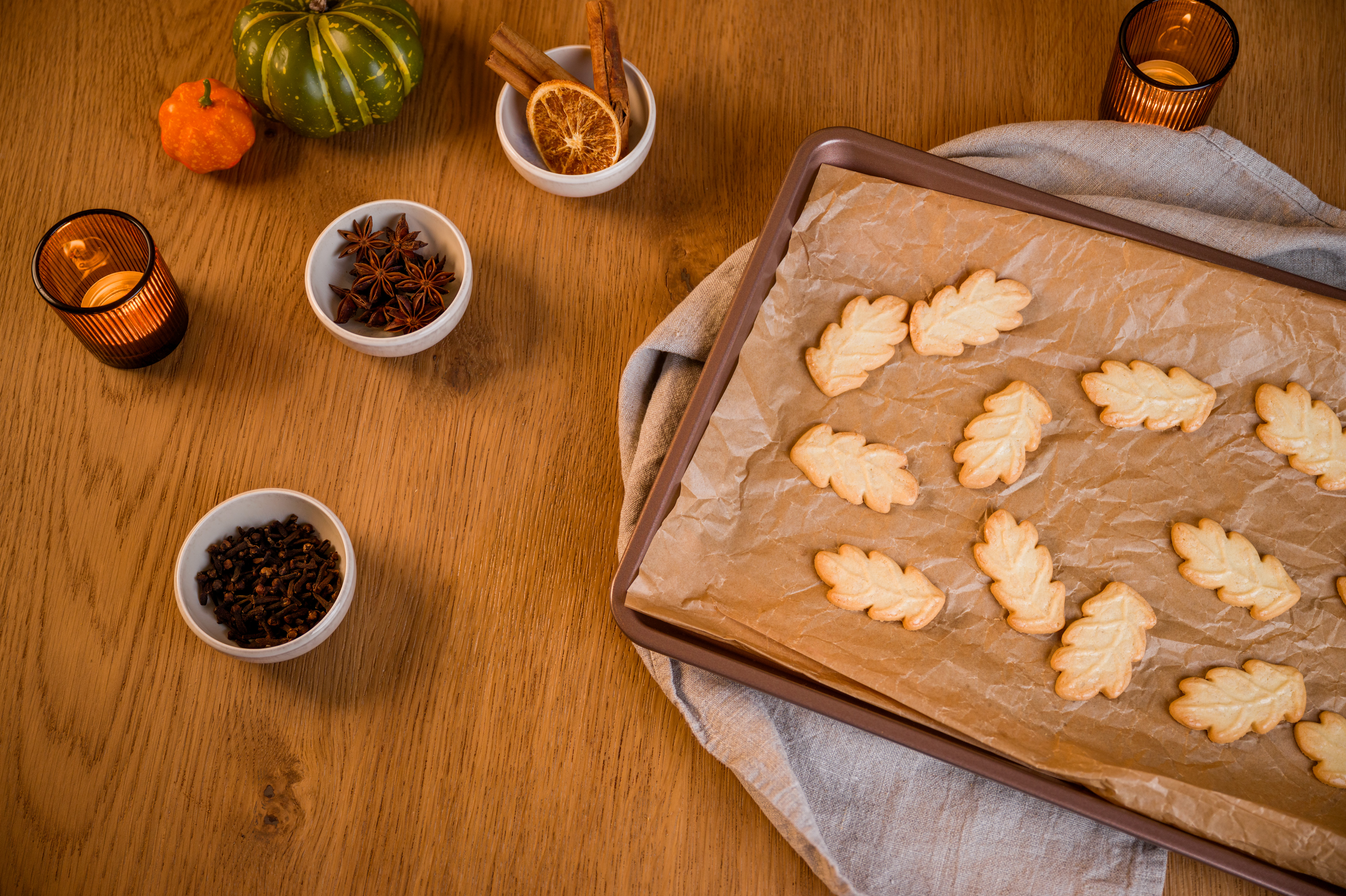 Auf einem Holztisch steht ein Backblech frisch gebackenen Plätzchen, umgeben von Gewürzen, Orangenscheiben und herbstlicher Dekoration