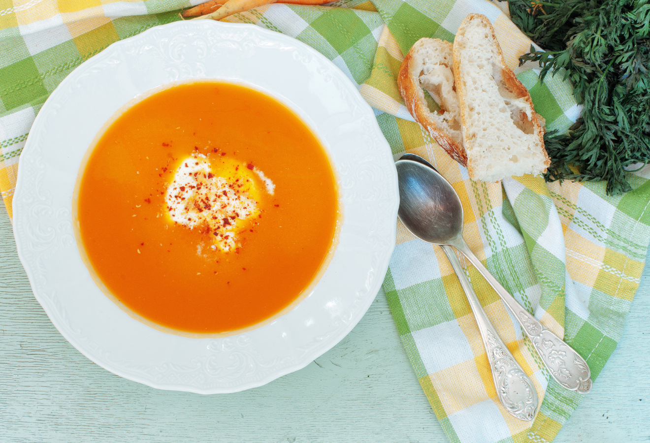 Möhren-Apfel-Suppe mit Ingwer-Vanille-Sahne in einem weißen tiefen Teller, daneben Brotscheiben und Löffel
