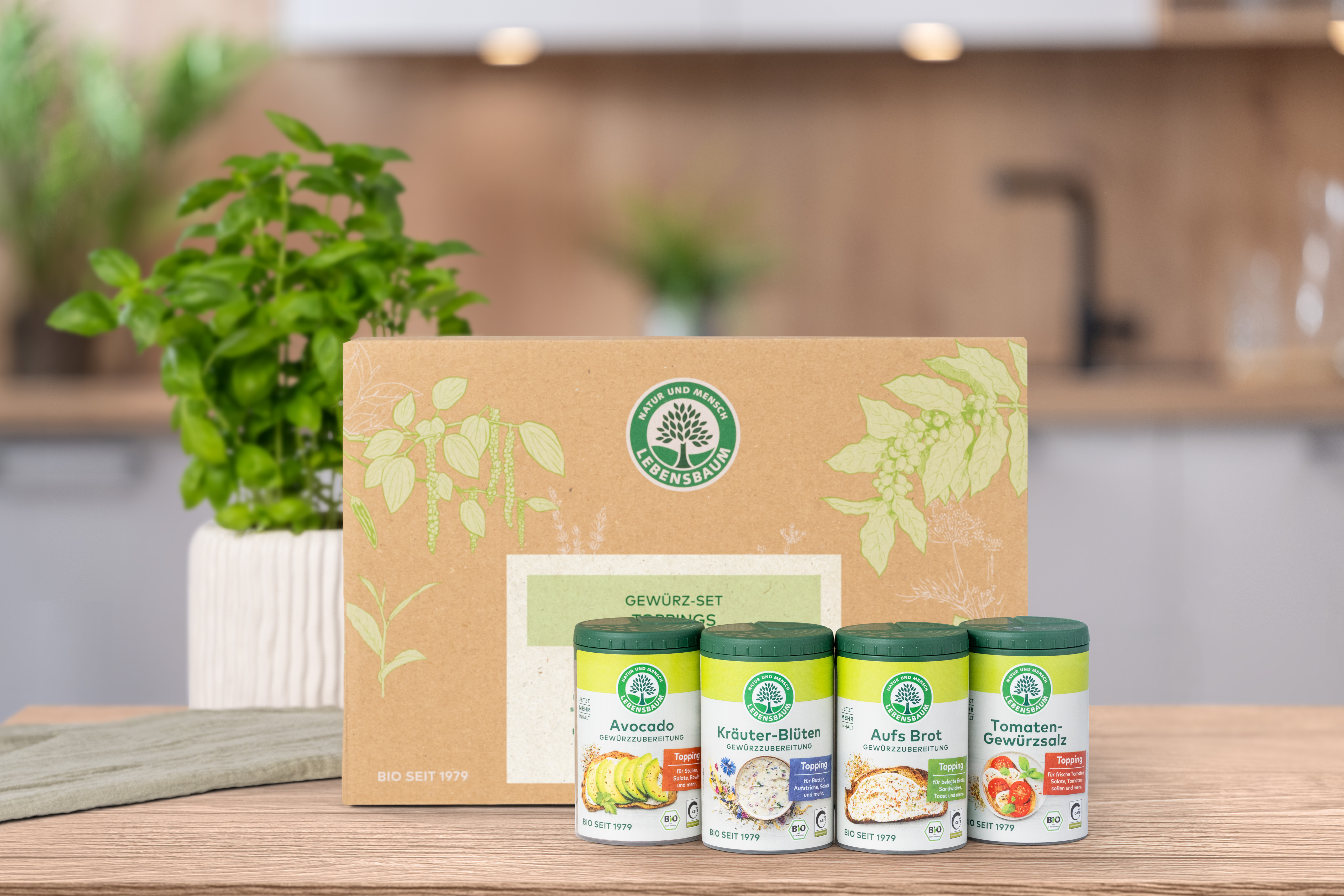 Verschlossenes Geschenk-Set steht auf einem Holztisch in der Küche. Vor der Geschenk-Set Verpackung  stehen die darin enthaltenen Produkte