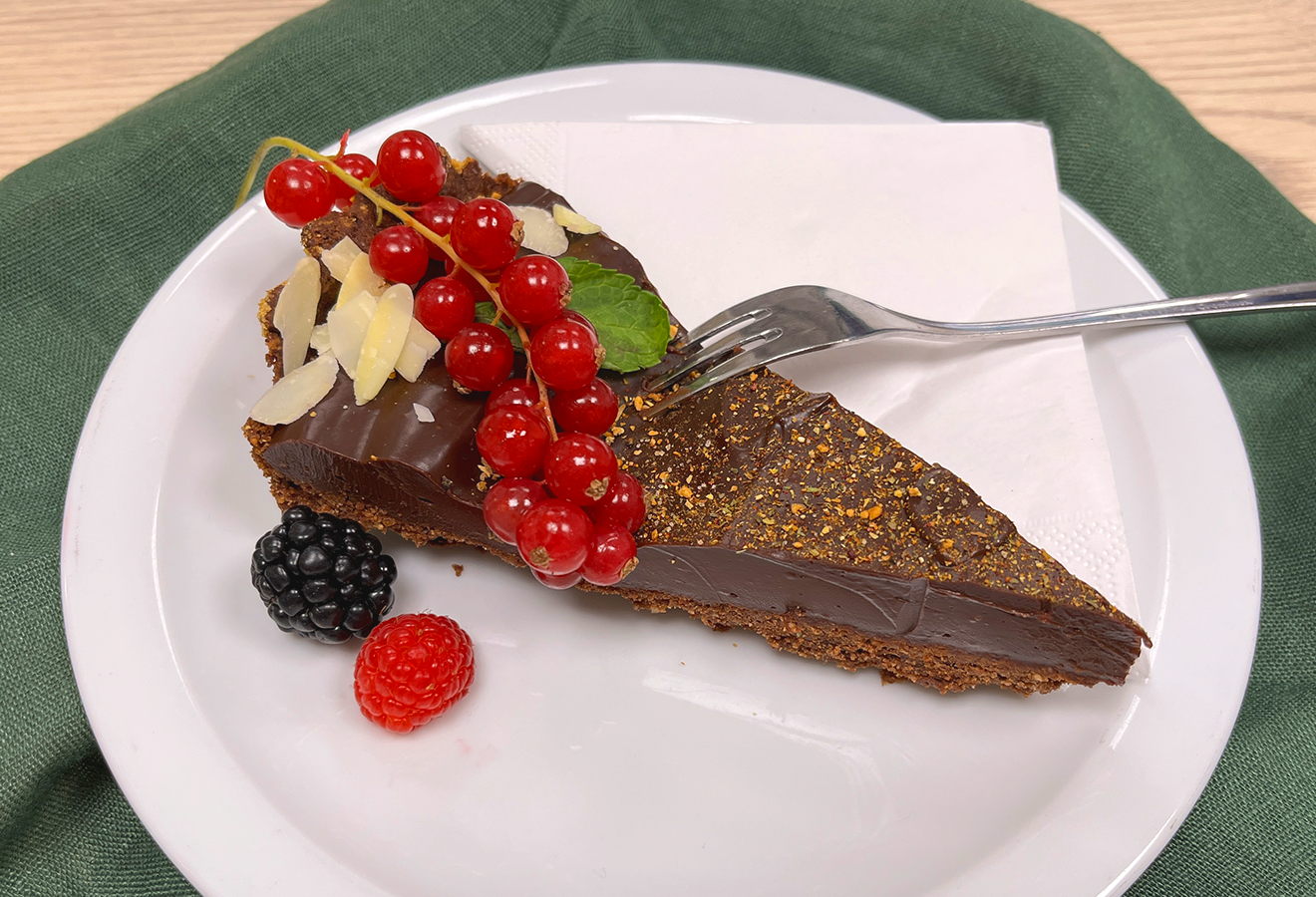Schokoladentarte auf einem weißen Teller, mit Beeren garniert, daneben eine Gabel
