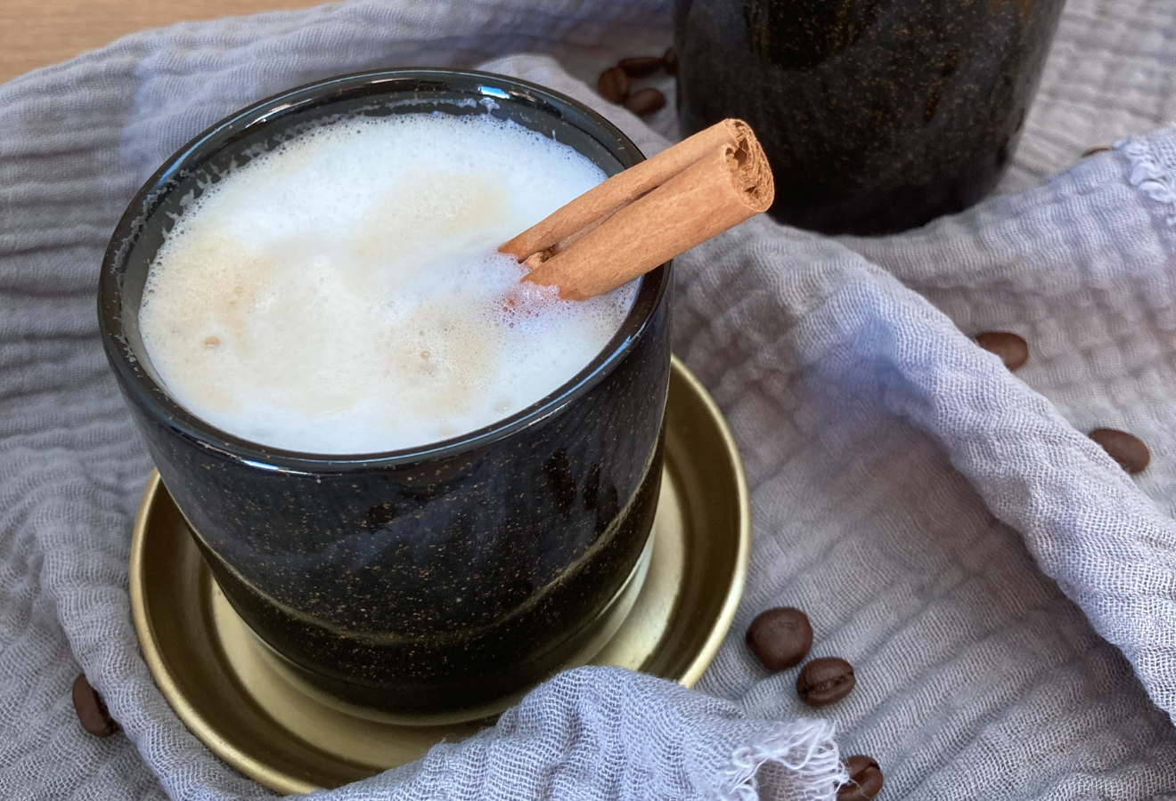 Milchkaffee á la gebrannte Mandeln in einer schwarzen Tasse mit einer Zimtstange darin