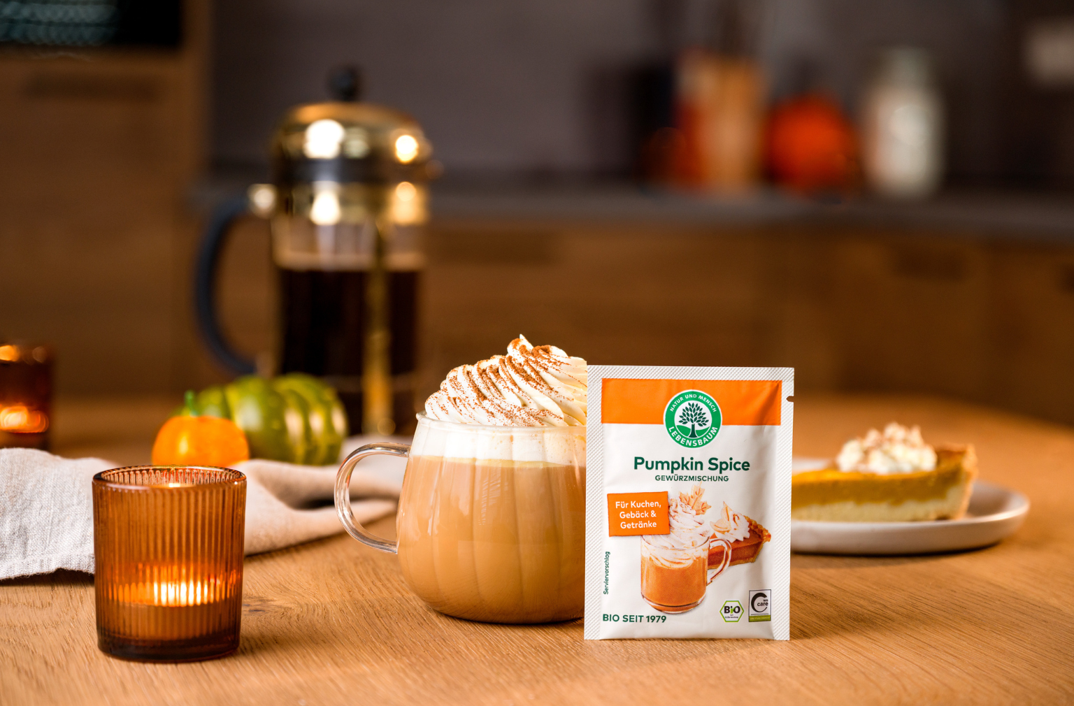 Pumpkin Spice Gewürzmischung neben einem Pumpkin Spice Latte mit Sahne auf einem herbstlich dekorierten Tisch