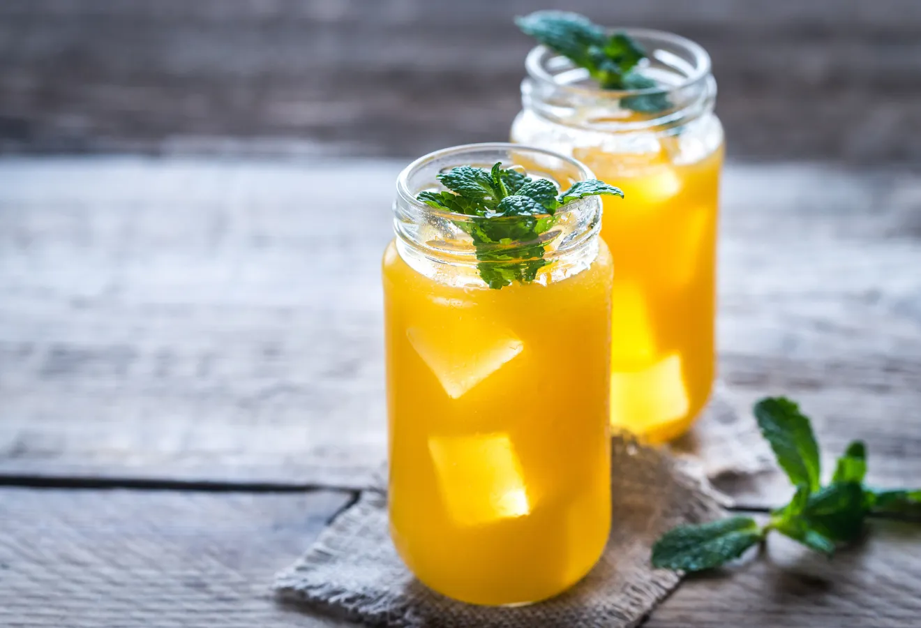 Ingwer-Mango-Eistee mit Vanille in 2 Gläsern mit Mangostücken und Minzblättern darin