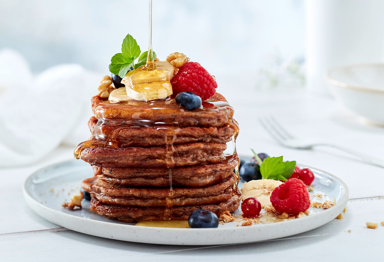 Würzige Bananen-Pancakes auf einem weißen Teller gestapelt, getoppt mit Obst und Honig