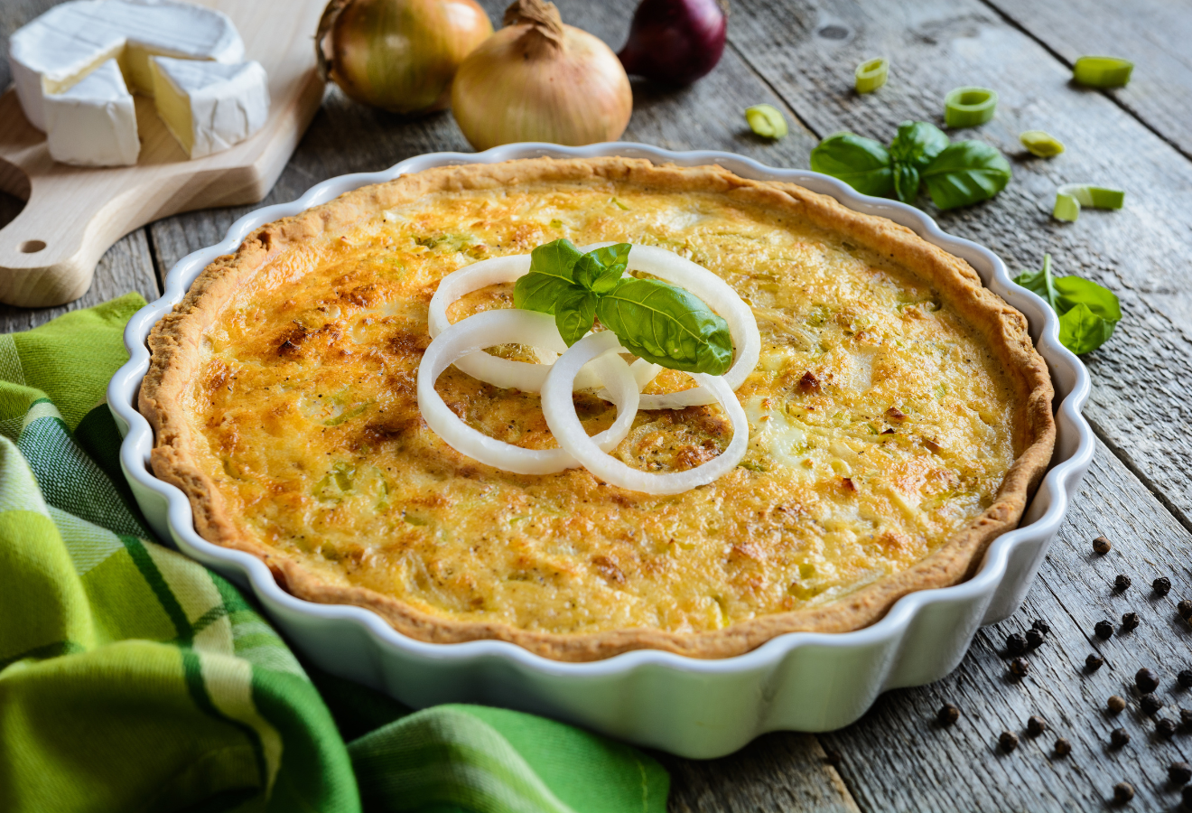Bärlauch-Zwiebel-Quiche in einer Quicheform mit Zwiebeln angerichtet