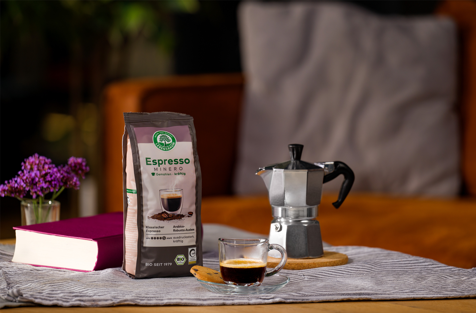 Packung Lebensbaum Espresso Mild steht neben einer Espressokanne und einer Tasse frisch gebrühten Espressos auf einem gedeckten Tisch