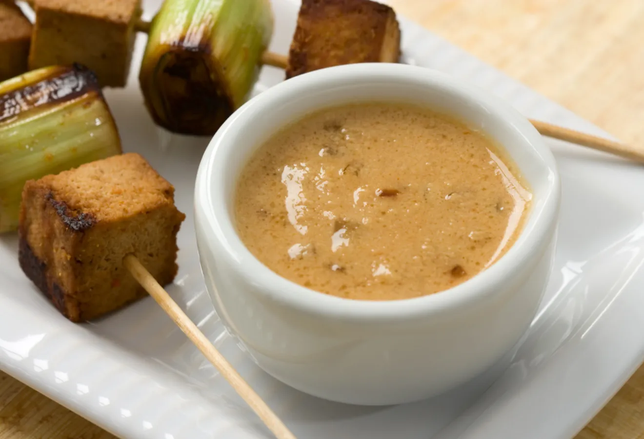 Erdnuss-Soße mit feiner Schärfe in einer weißen Schale, im Hintergrund Tofu-Spieße