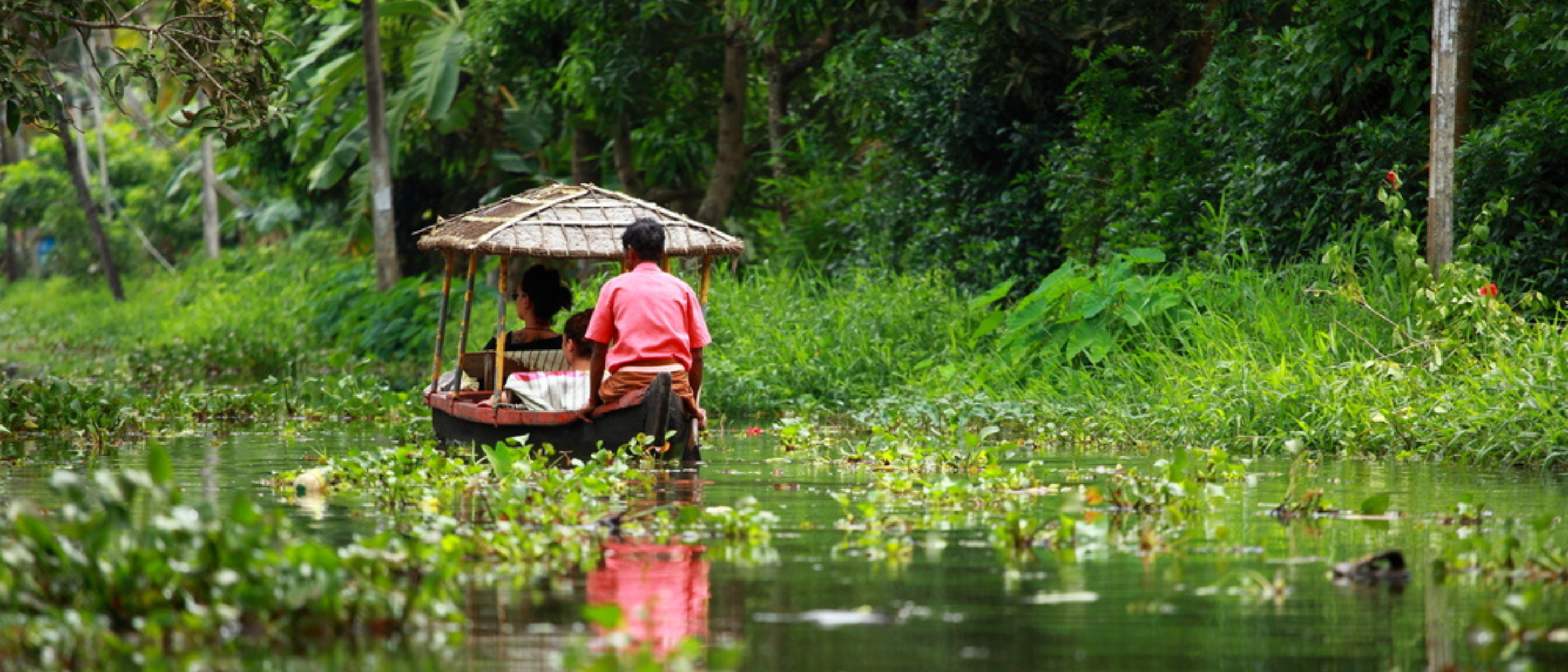 Fluss in Kerala, darauf zwei Menschen in einem kleinen Kanu