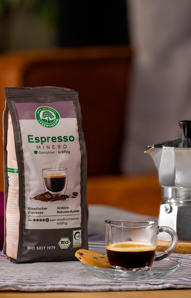 Packung Lebensbaum Espresso Mild steht neben einer Espressokanne und einer Tasse frisch gebrühten Espressos auf einem gedeckten Tisch