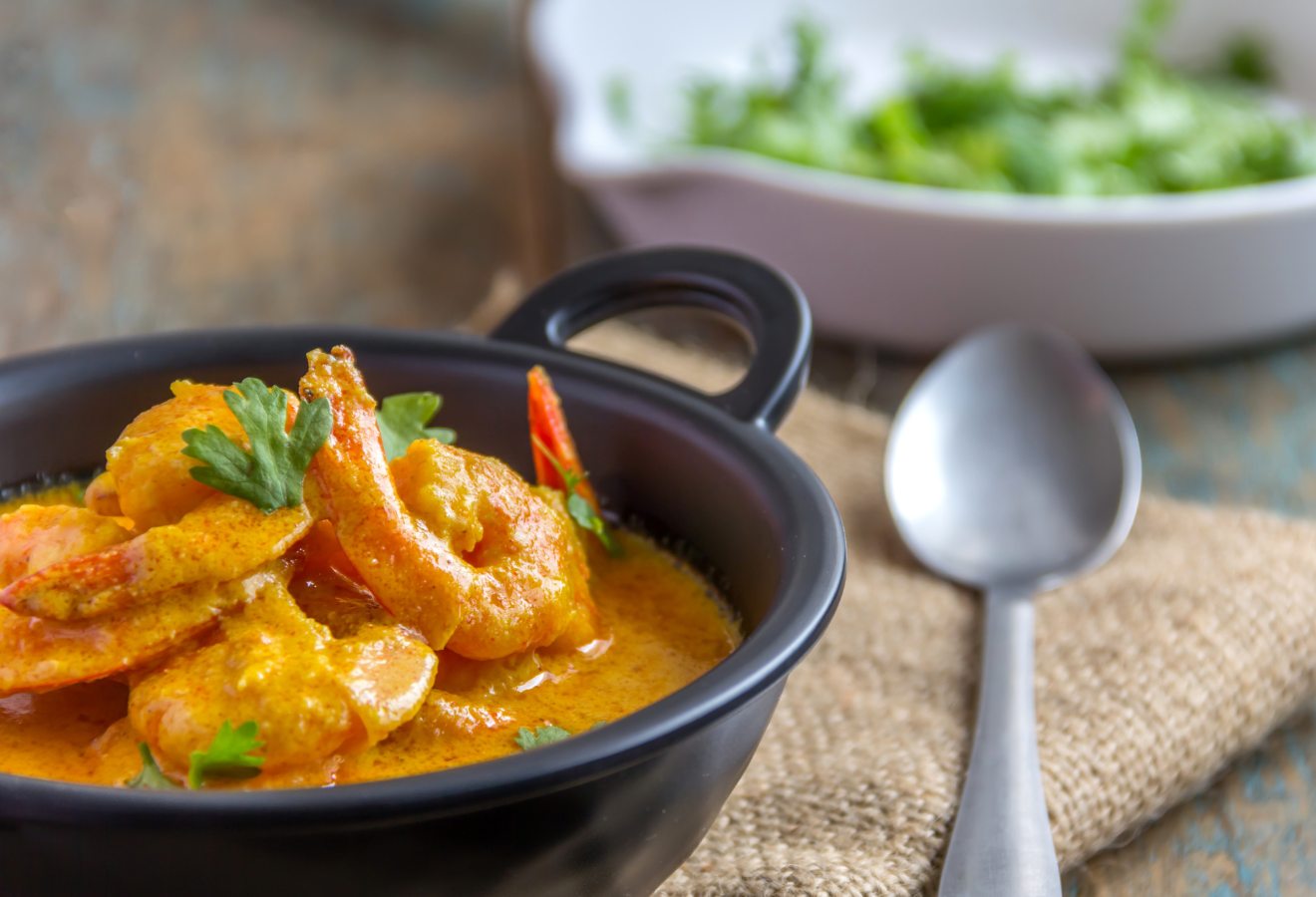 Currysuppe in einer schwarzen Schale mit einem Löffel daneben