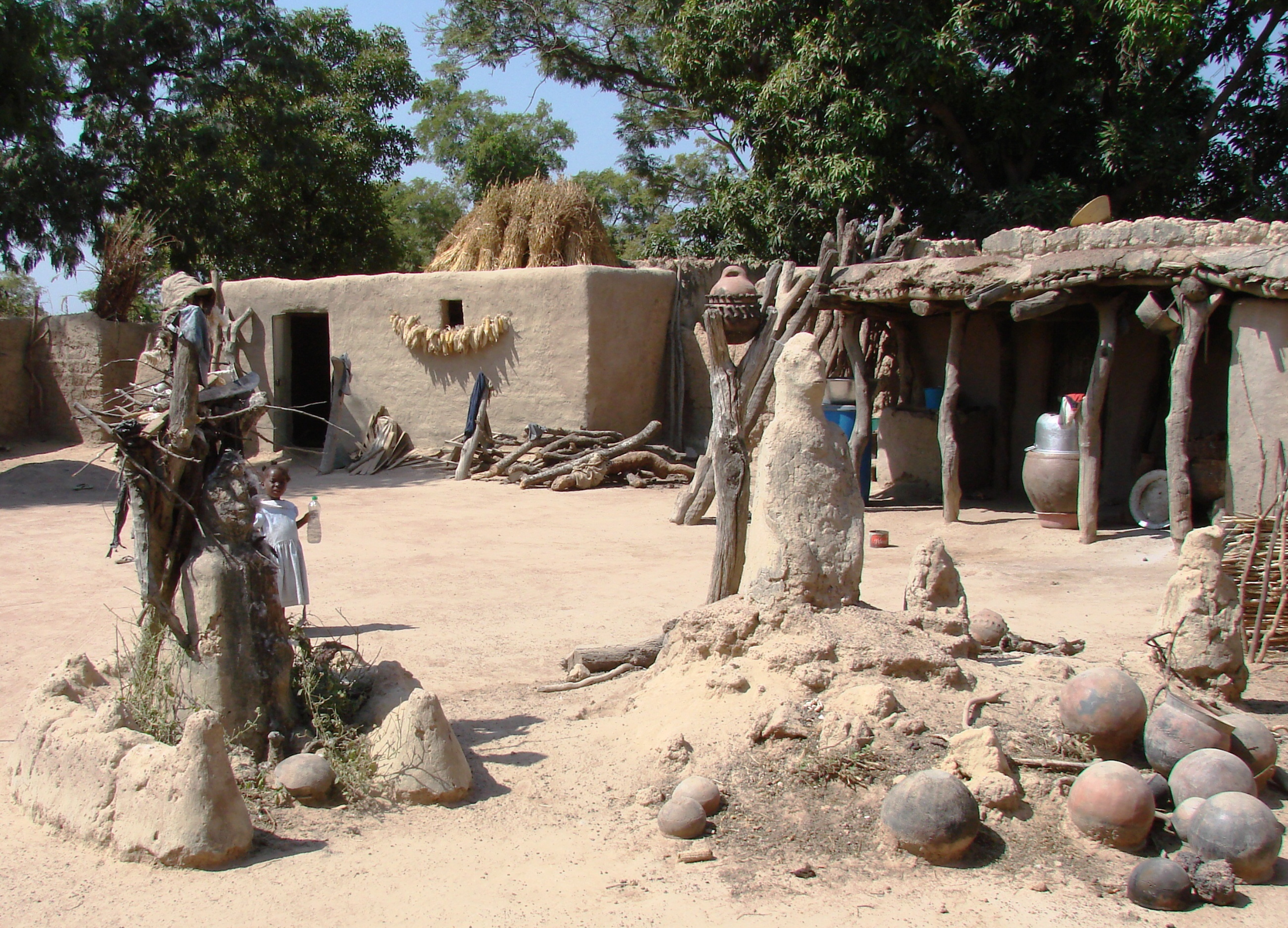 Traditioneller Hof mit Lehmhütten und Tonkrügen unter Bäumen in Burkina Faso