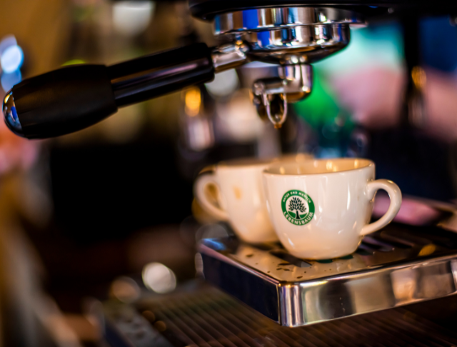Zwei weiße Tassen mit Lebensbaum Logo stehen unter einer Espressomaschine, bereit zum Befüllen