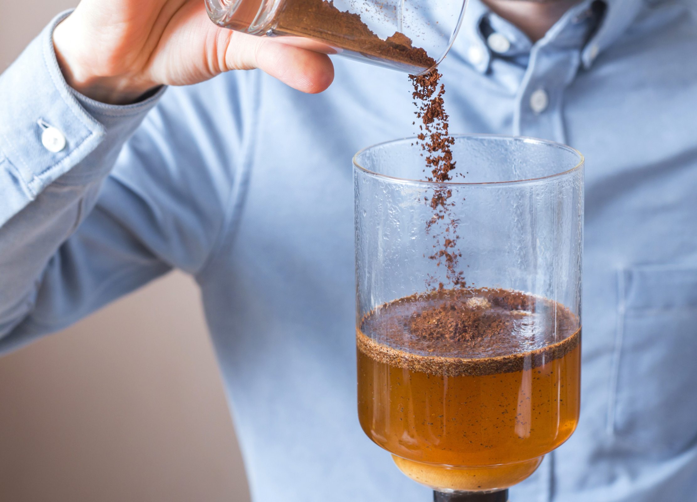 Kaffeepulver wird in den oberen Glasbehälter eines Syphon-Kaffeebereiters geschüttet, wo es sich mit heißem Wasser vermischt