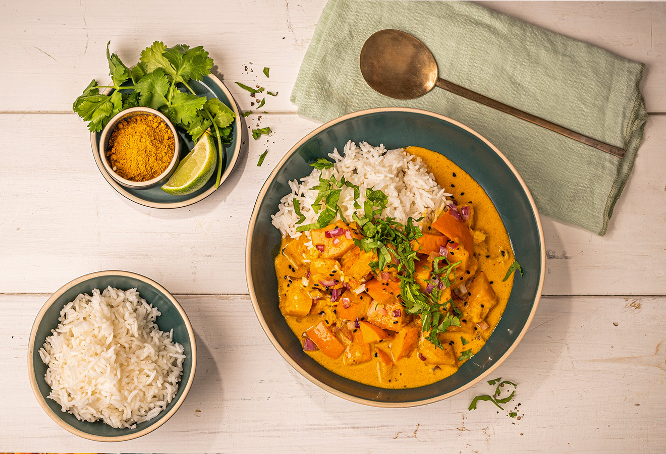 Kürbiscurry in einer Schale, daneben ein Schälchen Reis